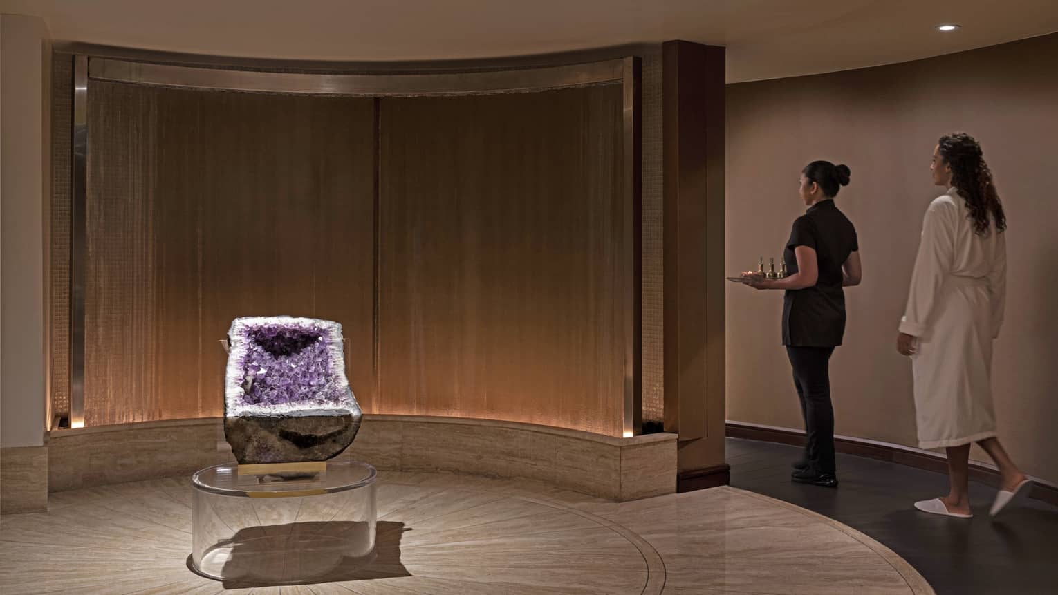 A spa team member walking with a woman in a spa robe.