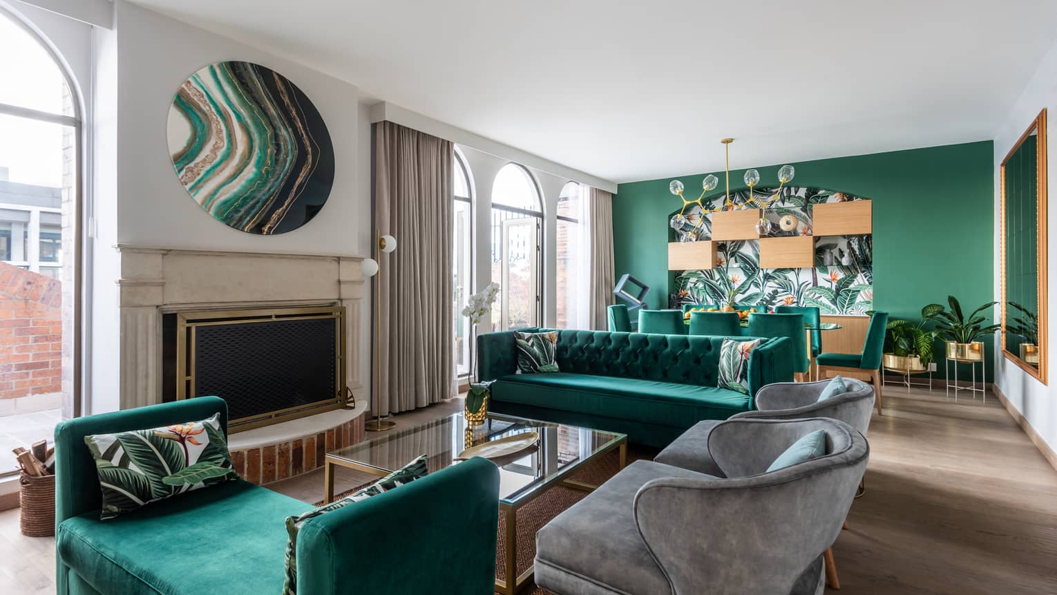 A sitting area with several emerald green couches, small grey chairs and plants.
