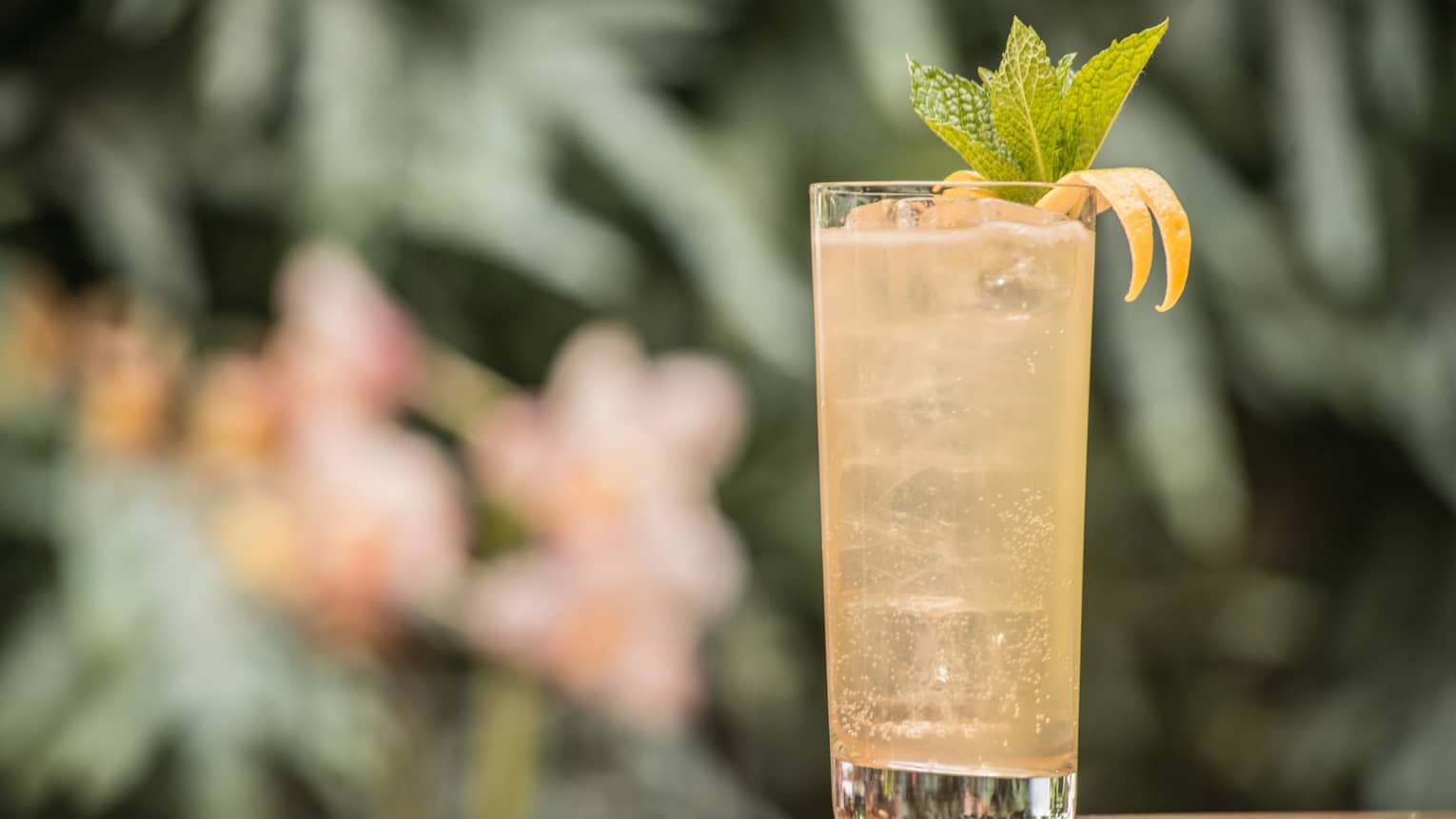 A tall glass filled with a yellow cocktail and several mint leaves. 