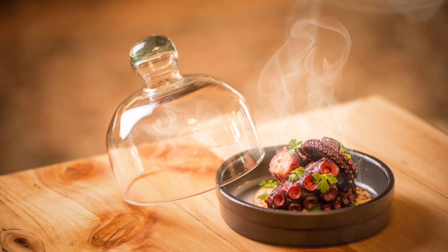 Steam rises from Grilled Octopus in round black dish with glass lid