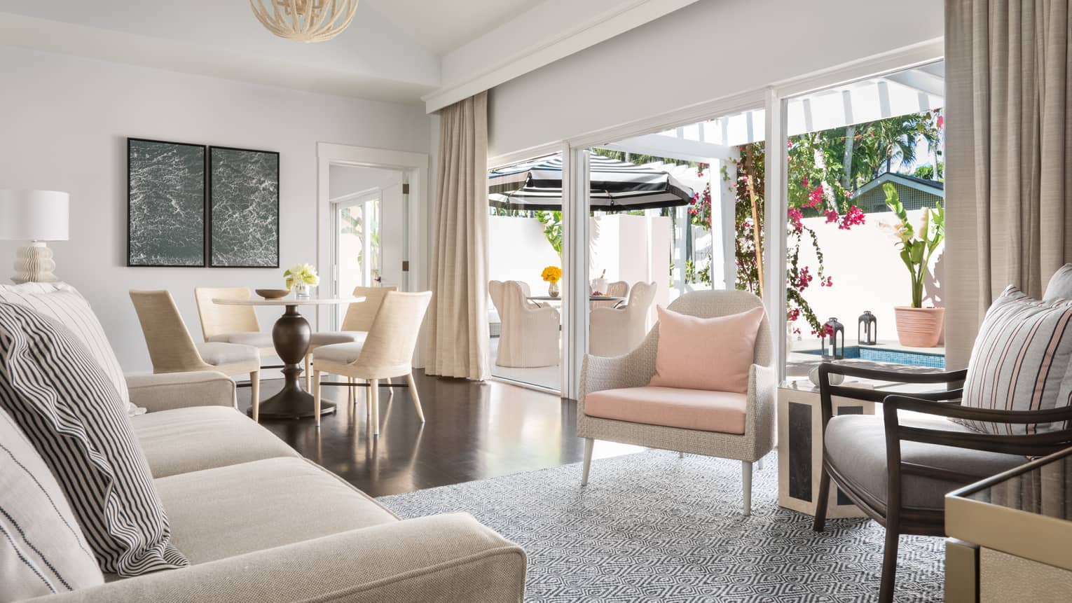 Plunge pool living room with neutral tones, featuring a sofa, dining table and sliding doors opening to an outdoor patio with seating and vibrant flowers