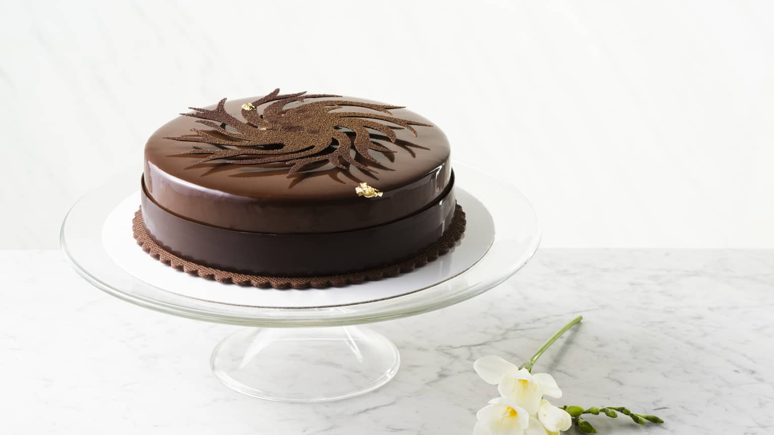 Round Gresham signature chocolate cake on glass cake plate and daffodils on table