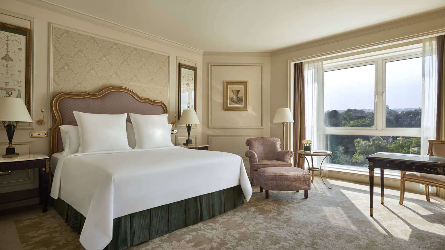 Deluxe Room bed with upholstered pink headboard, gold pattern wallpaper, pink silk armchair by sunny window