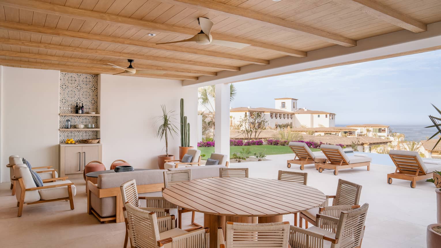 Covered outdoor terrace with large round dining table, sofa, chairs and sun loungers by a pool at Four Seasons Resort Cabo San Lucas at Cabo Del Sol