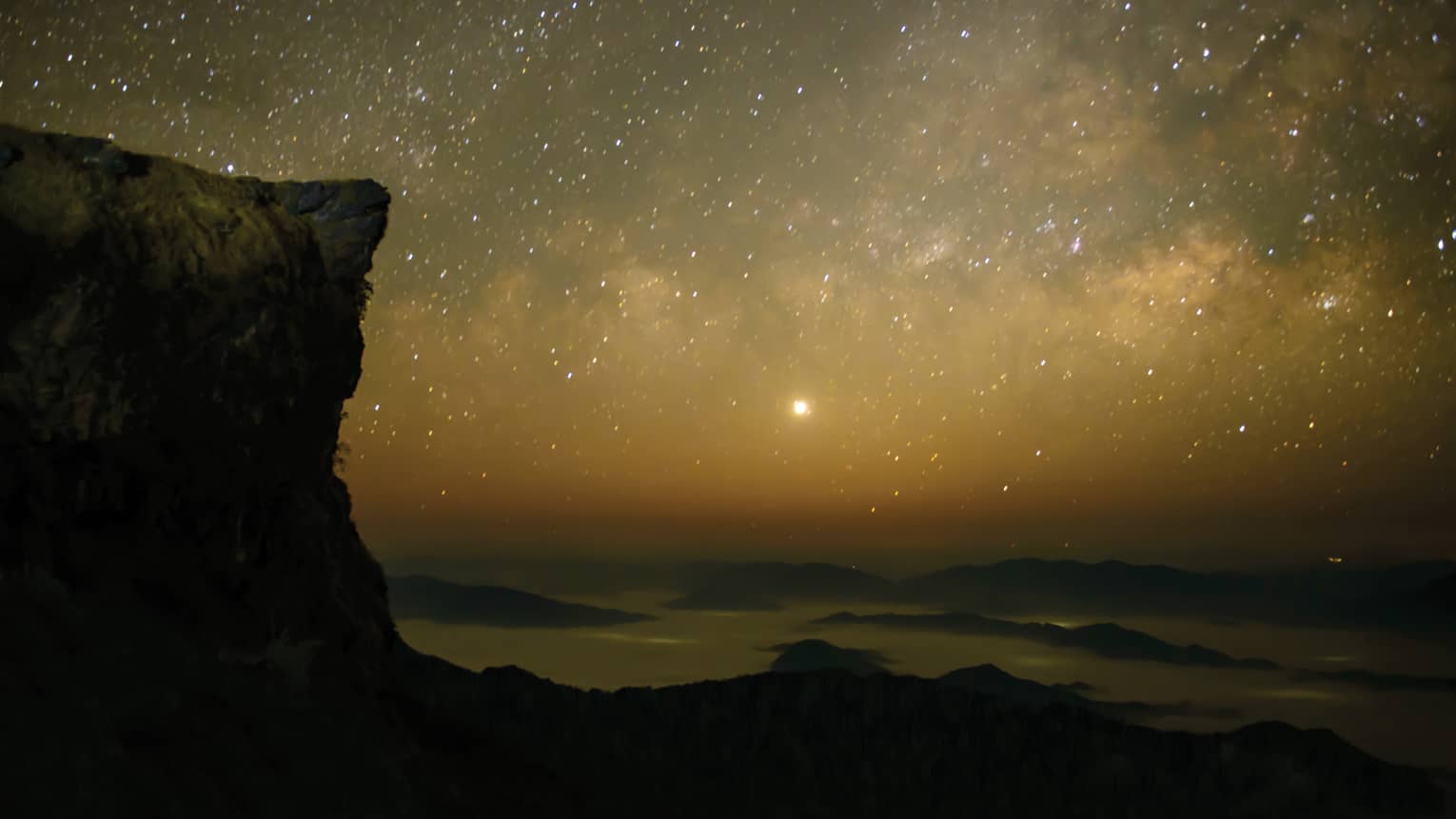 View of night sky with stars over the ocean, cliff edge in forefront