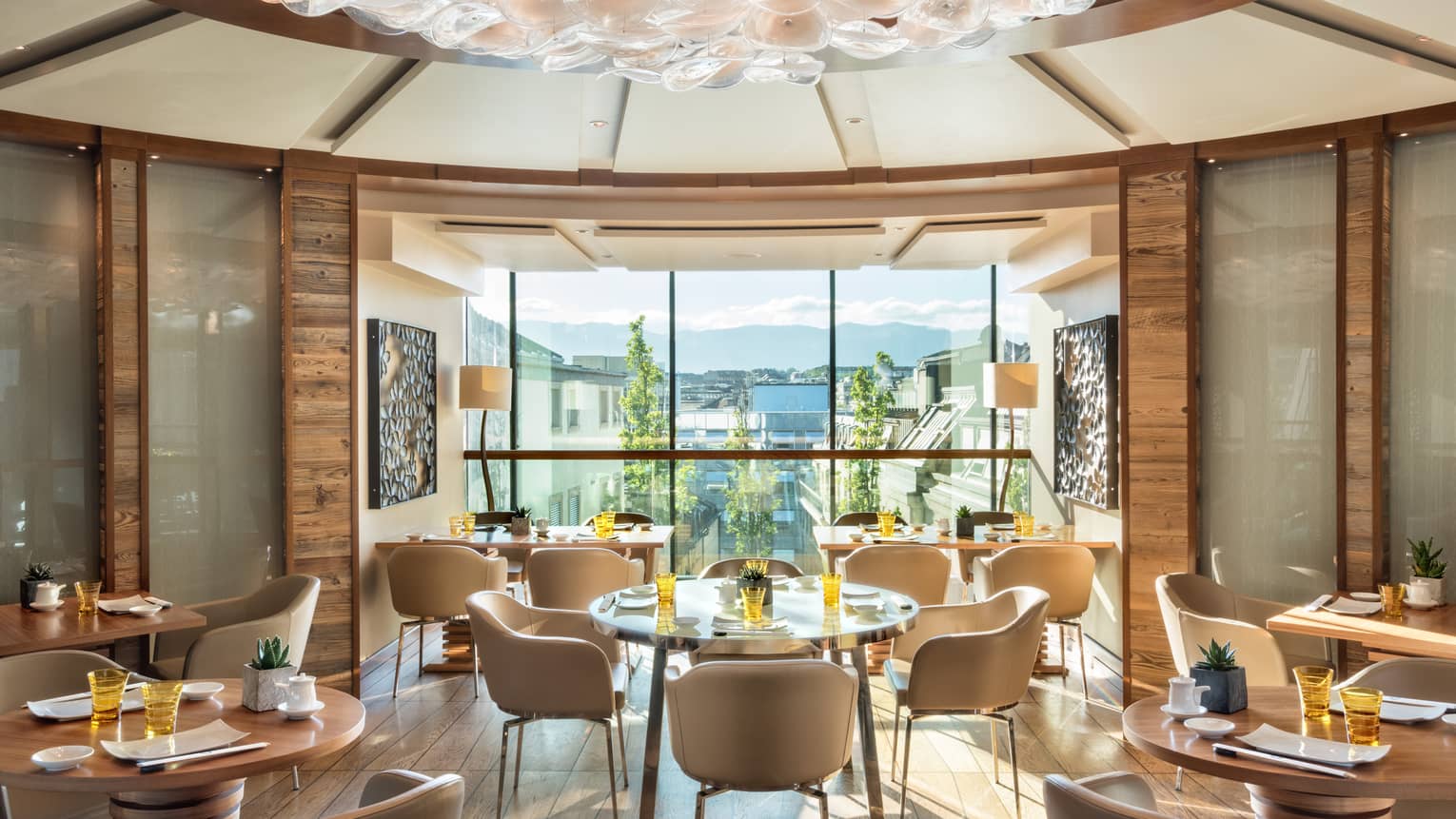 Sunny rotunda dining room with cream-coloured chairs, round wood tables, floor-to-ceiling window