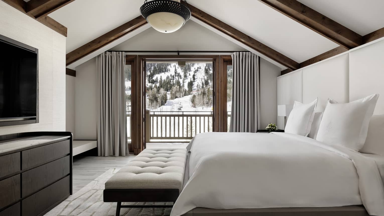 Bedoom with king bed and upholstered bench, dresser, TV and mountain-view balcony