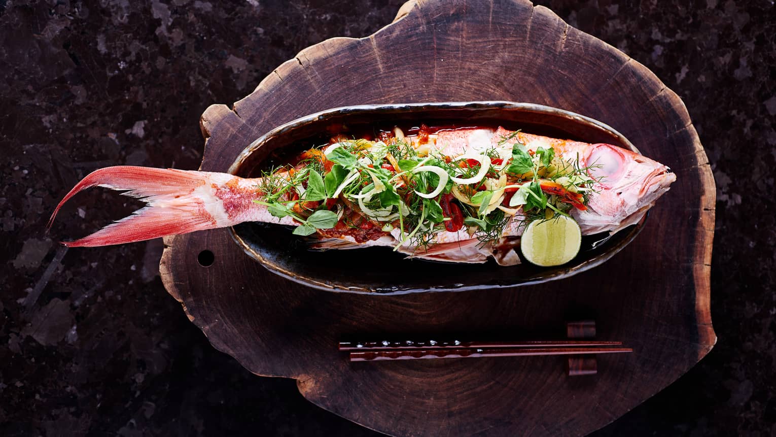 Whole grilled fish on skillet with fresh greens, vegetables, lime