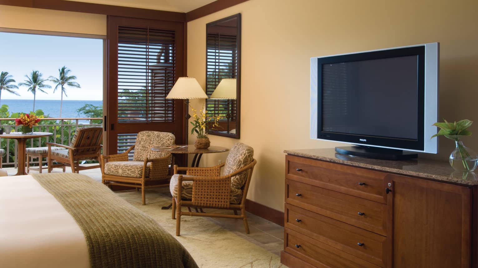 Oceanfront Room end of bed with folded wood blanket, dresser with TV, table and chairs by patio