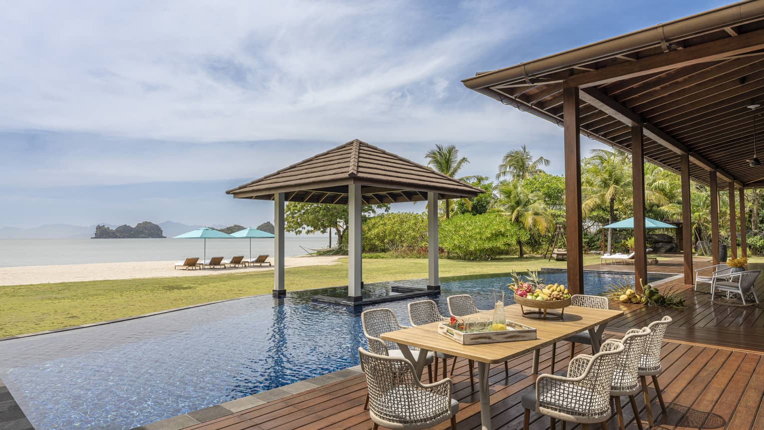 Pool deck with dining table, pool, covered lounge area and beach view