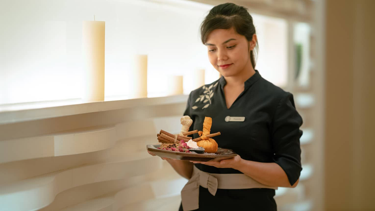 Spa staff member holds plate with aromatics, including cinnamon stick, rose petals and ginger root