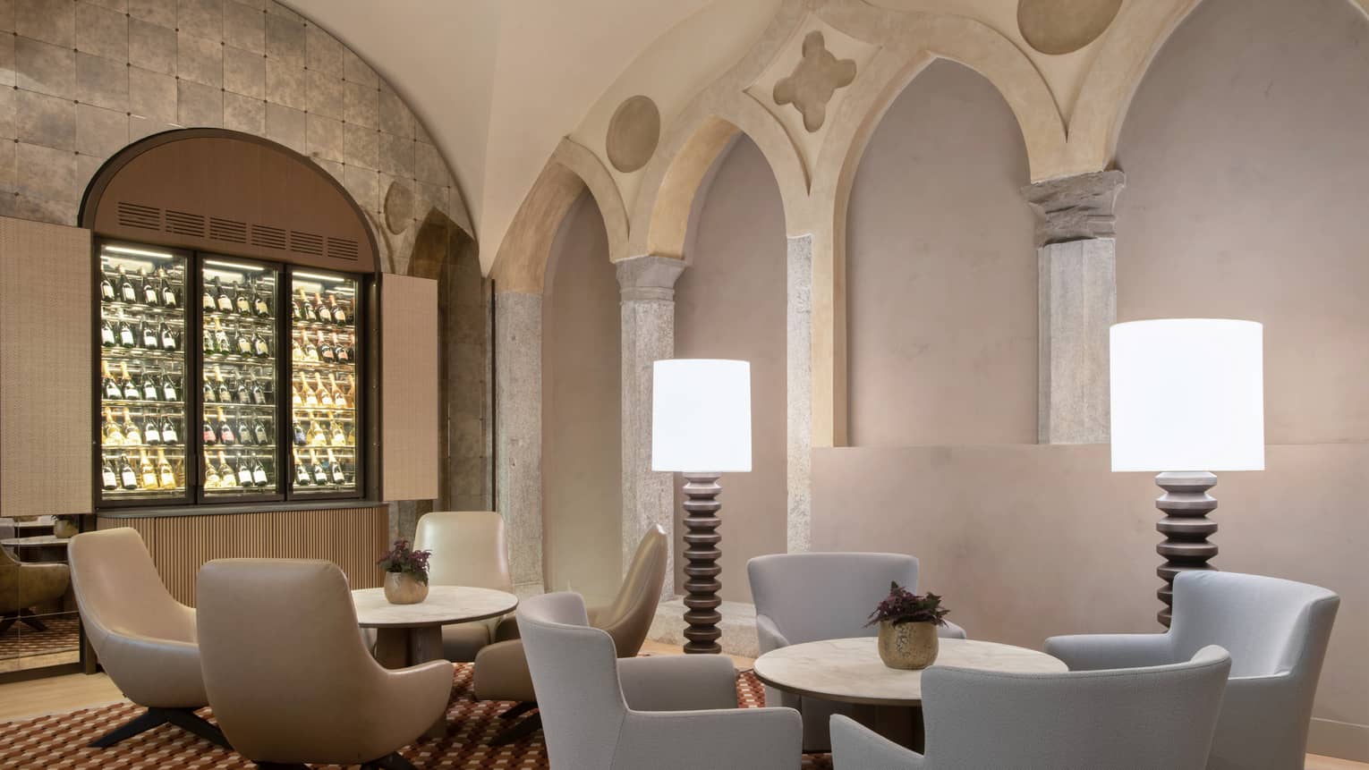 Camino lobby bar with neutral modern round tables and chairs, two floor lamps, arches in backdrop