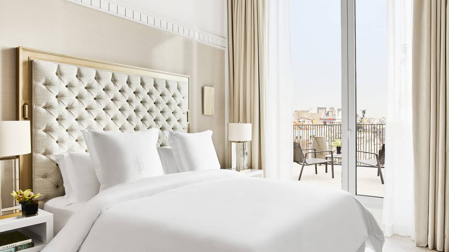 Luxury hotel suite bedroom with a king bed, tufted headboard, bedside lamps and access to a private terrace with city views