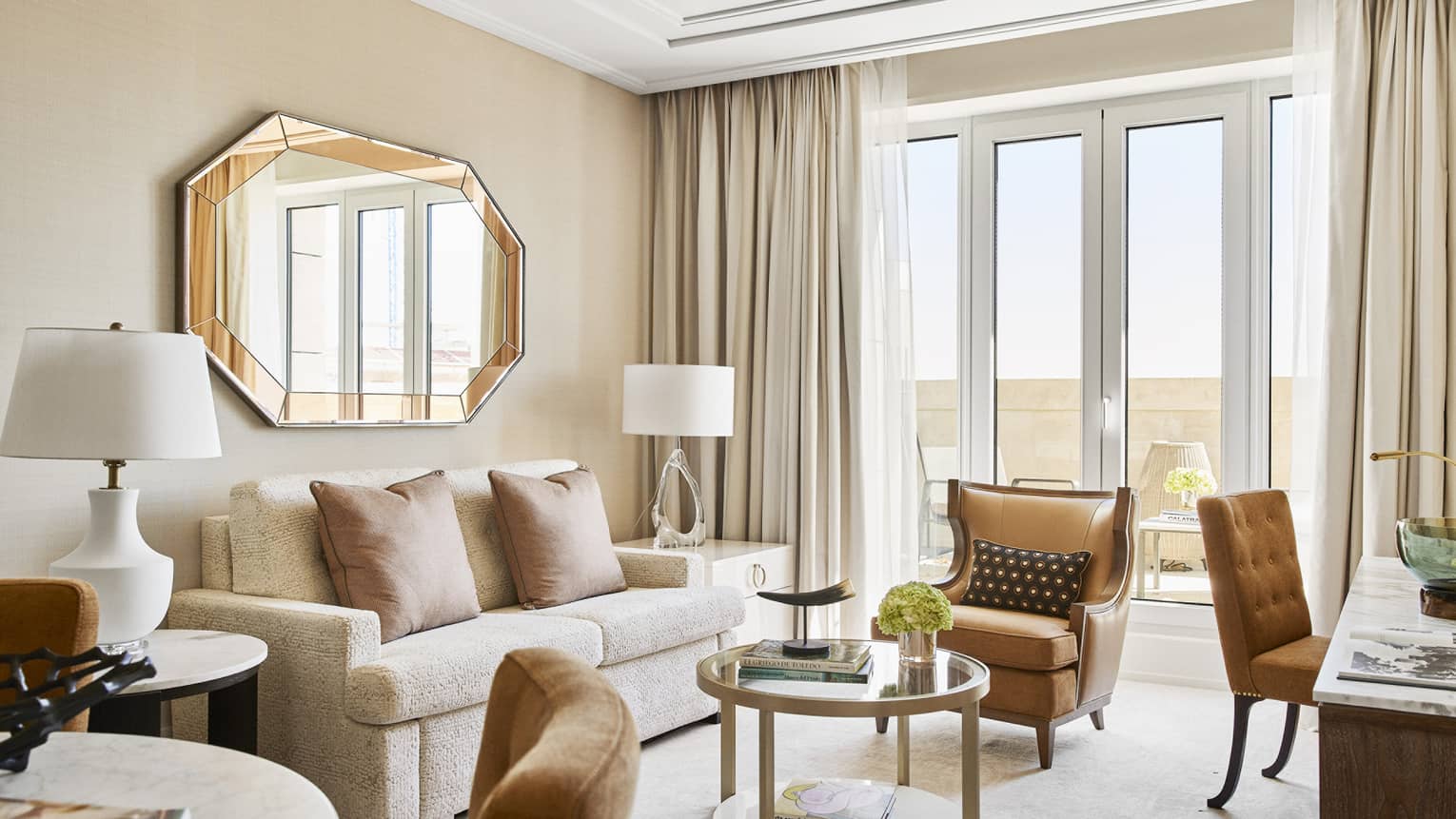 Four Seasons suite living room with a cream sofa, armchair, coffee tables, chairs, decorative octagonal mirror and floor-to-ceiling windows opening to a terrace