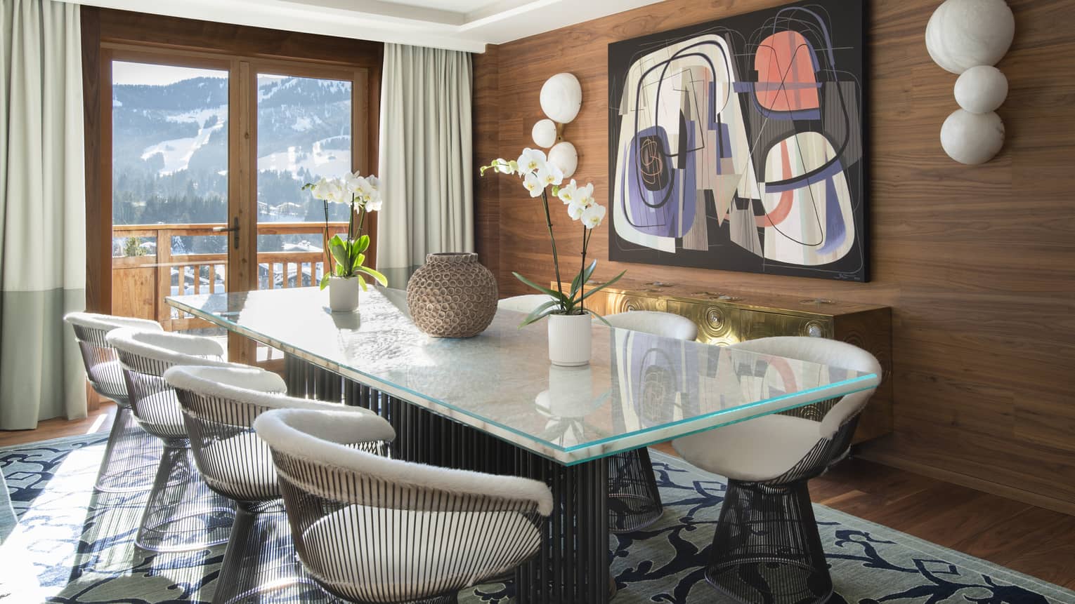 Wood-panelled dining room with modern art, rectangular glass table and round metal chairs, and mountain views