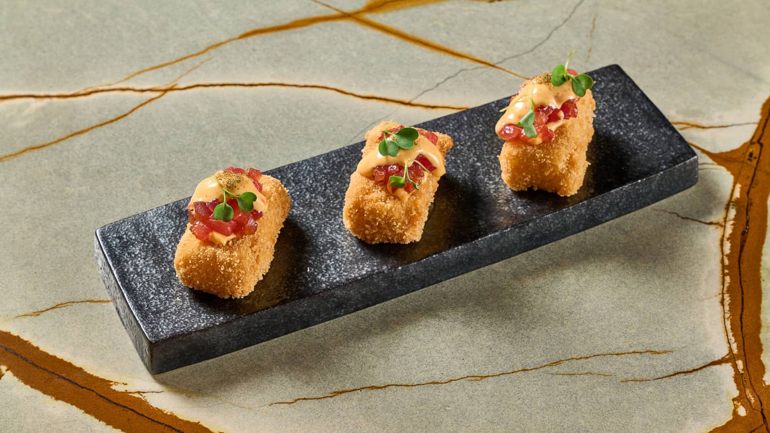 Three pieces of tuna crispy rice served on a rectangular black patter