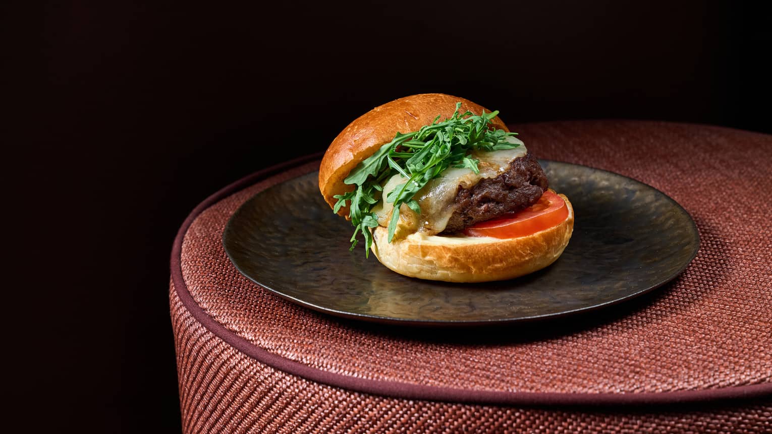Cheeseburger served on a black plate set on top of a brown rattan table