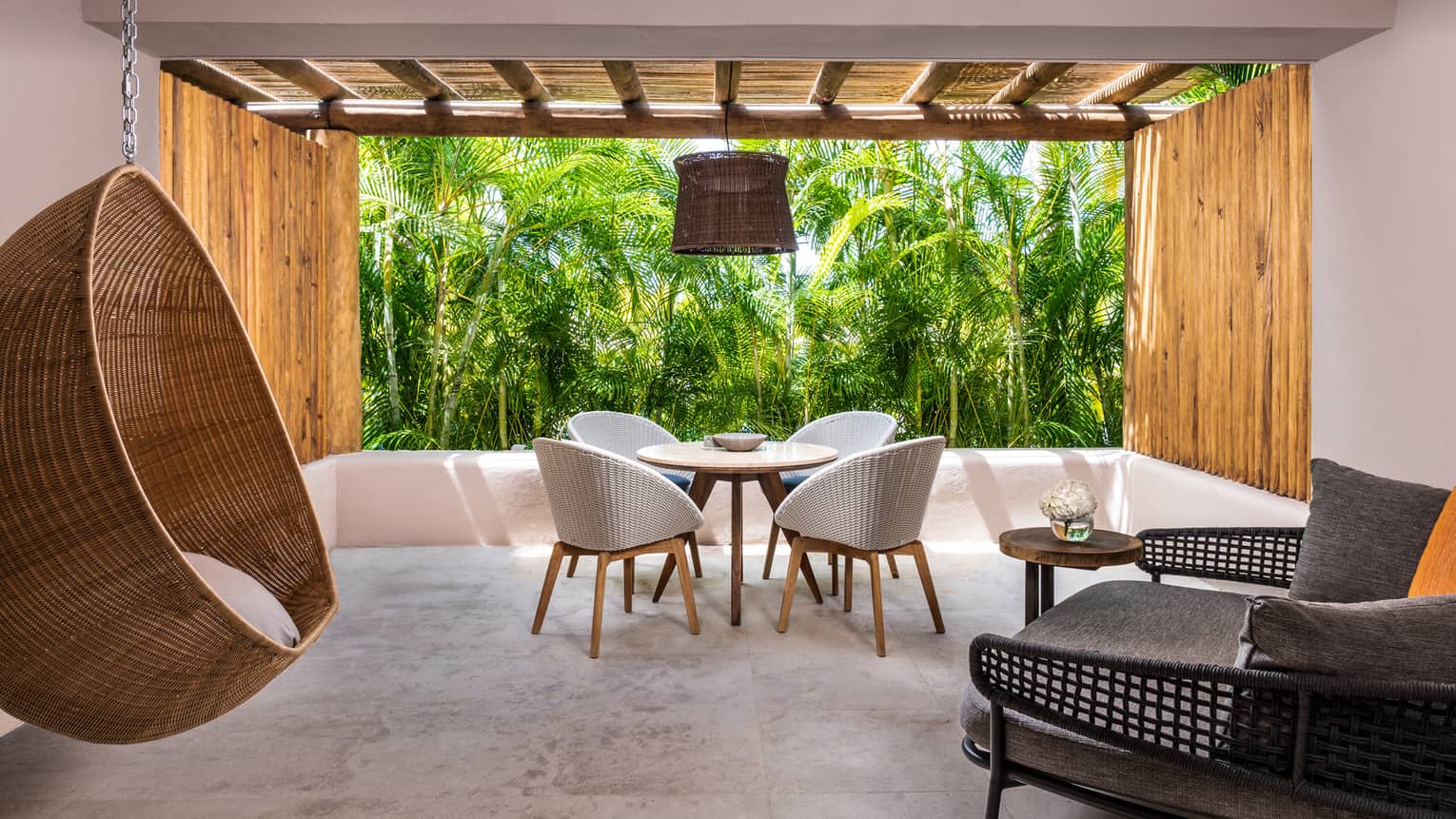 Indoor-outdoor living room with table for four, hanging whicker chair, palm trees