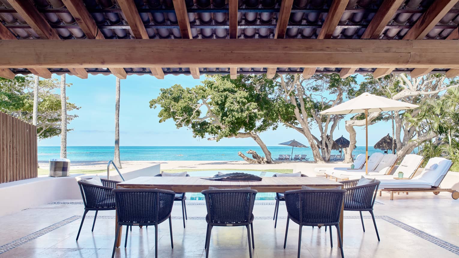Arena Beach House open-air dining area with rectangular table, eight rattan chairs, portico for shade