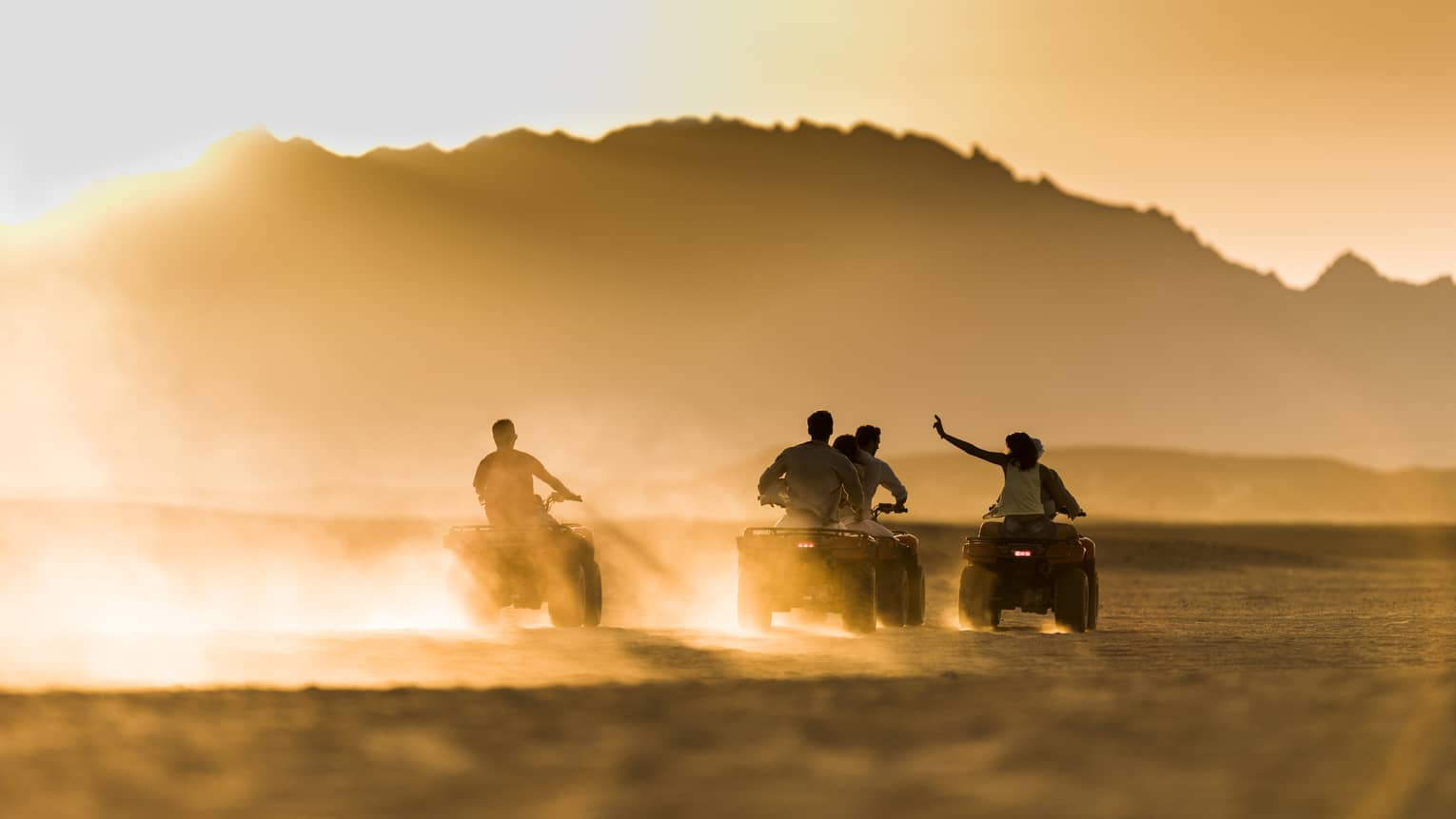 A group of people speed across the desert by e-quad