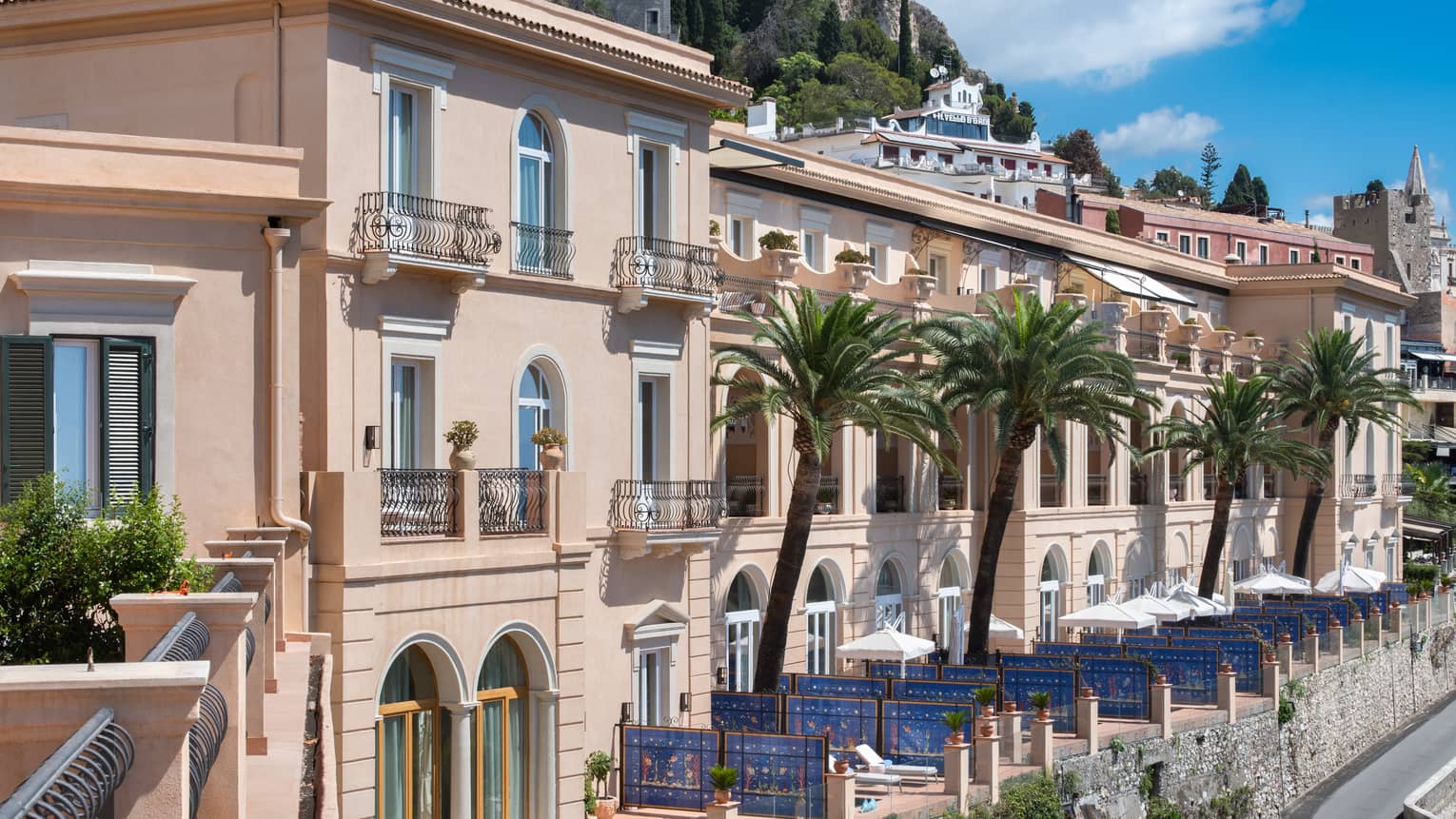 Hotel Exterior with palm trees, blue skies, rolling green hills in background