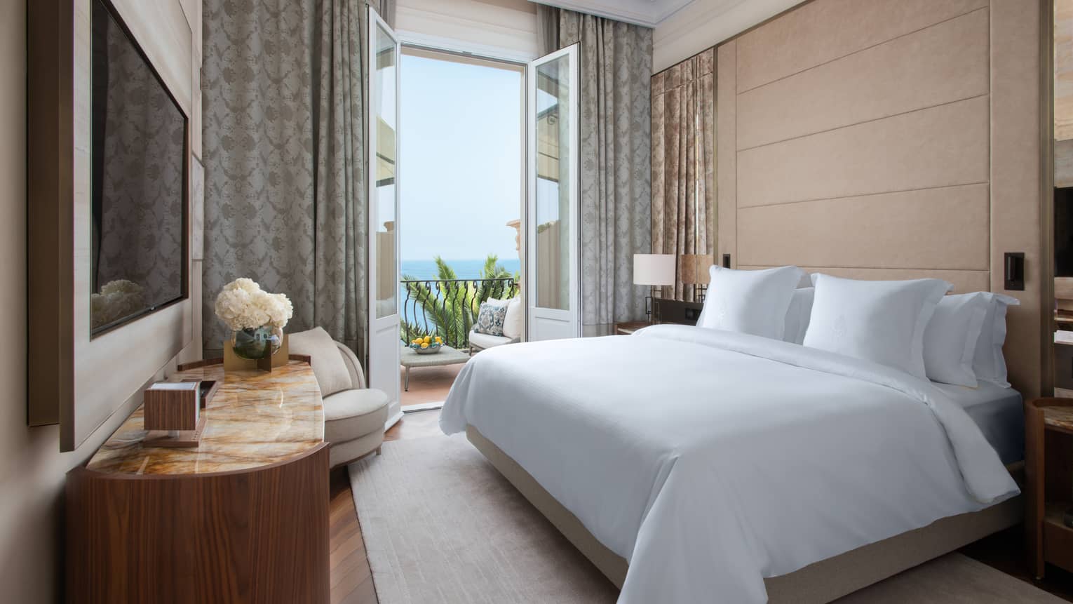 Royal Suite with king bed, white linens, flat screen TV, French doors leading to balcony with view of the Mediterranean Sea