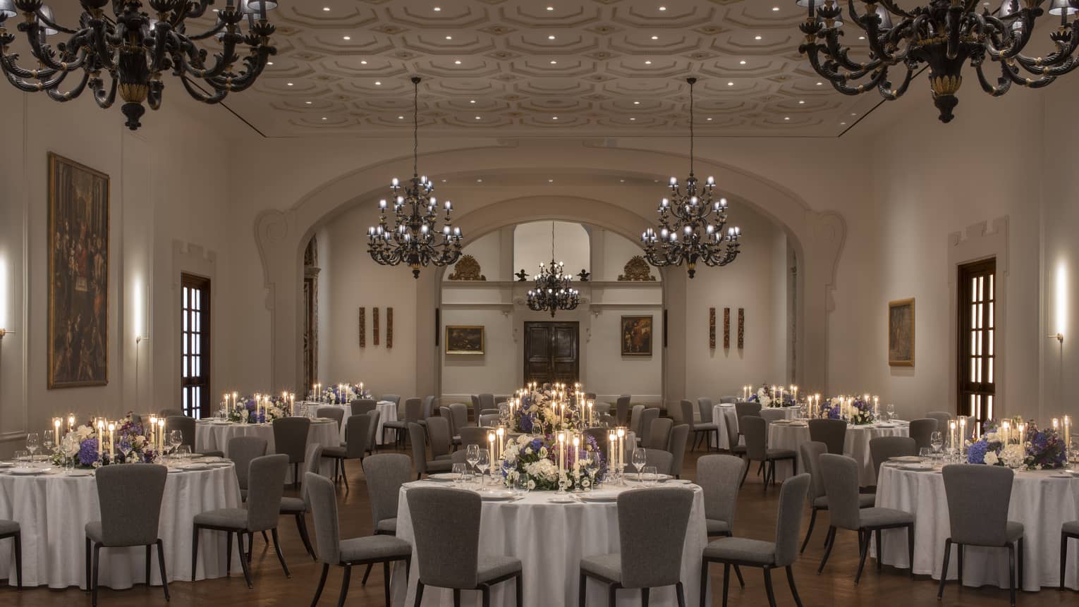 Elegant ballroom with round tables and chairs arranged for a wedding, adorned with large chandeliers above
