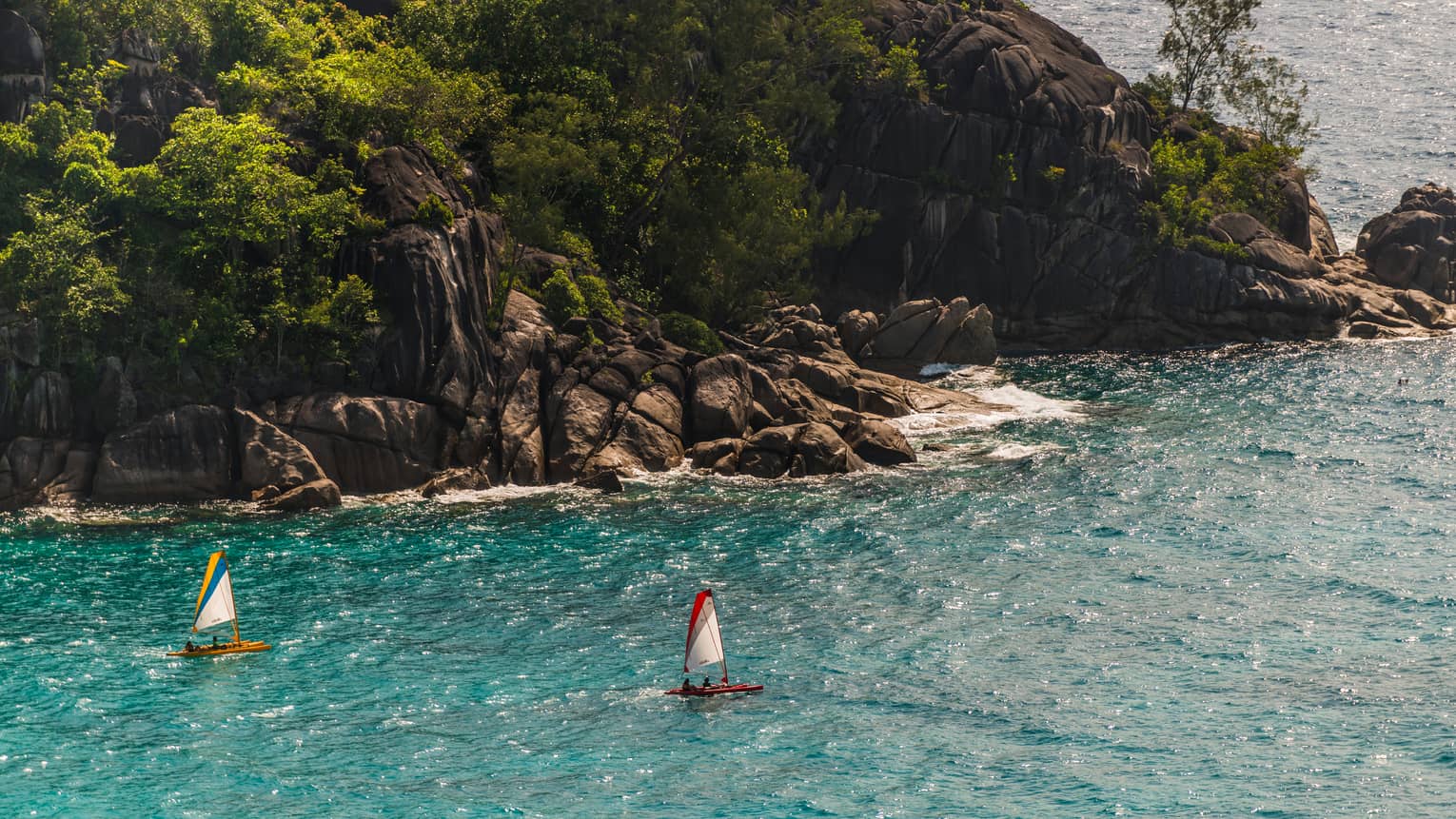 Aerial view of two sailboats in turquoise lagoon in front of rock cliffs, green trees