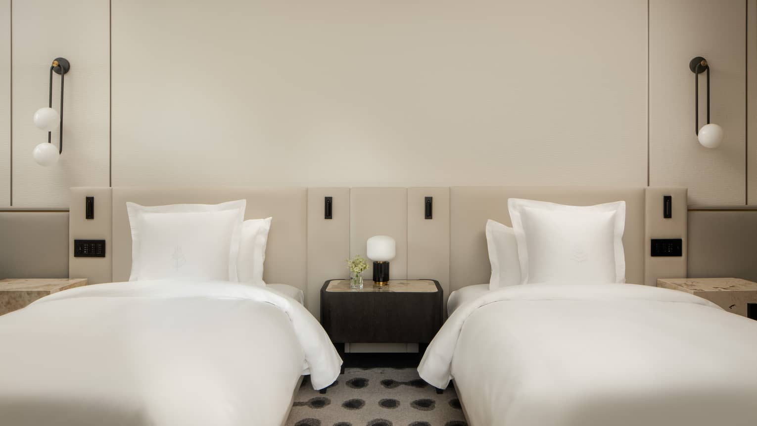 Luxury hotel room with two double beds, white linens, a shared nightstand, wall-mounted lights, featuring minimalist décor 