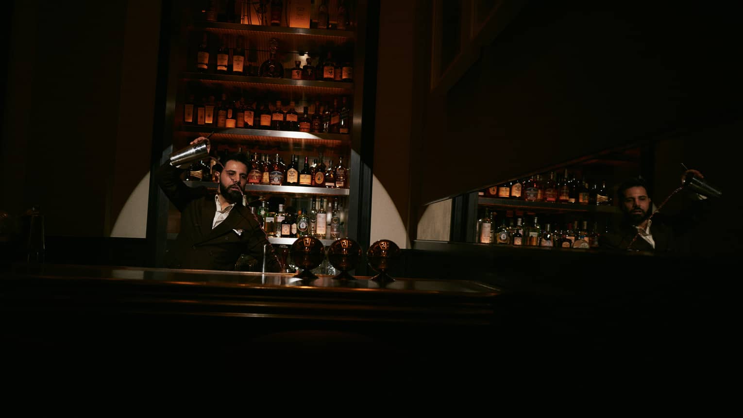 Bartender shakes a cocktail shaker behind a dimly lit bar
