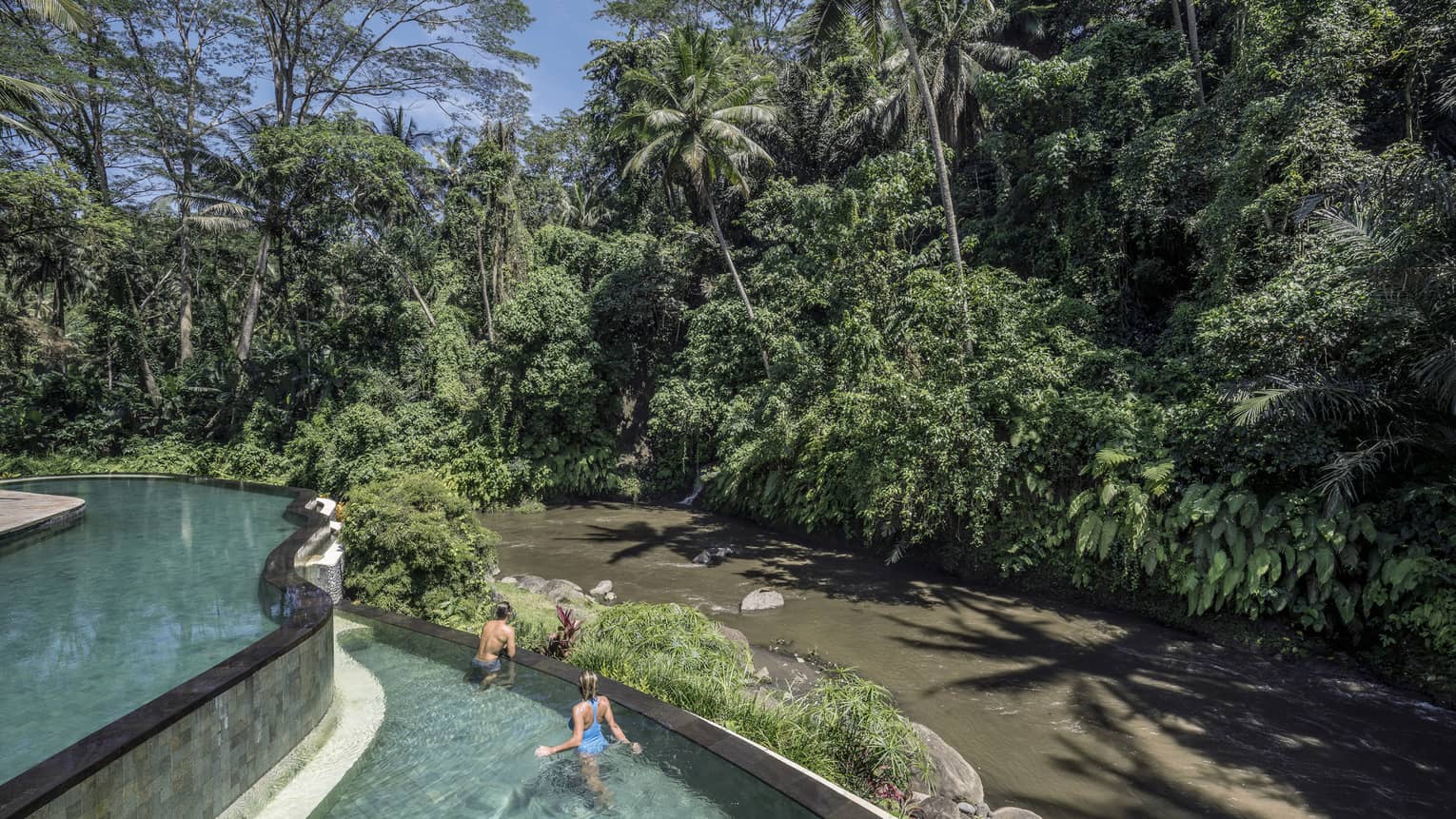 Hotel guests swimming in a pool, overlooking a river in Bali