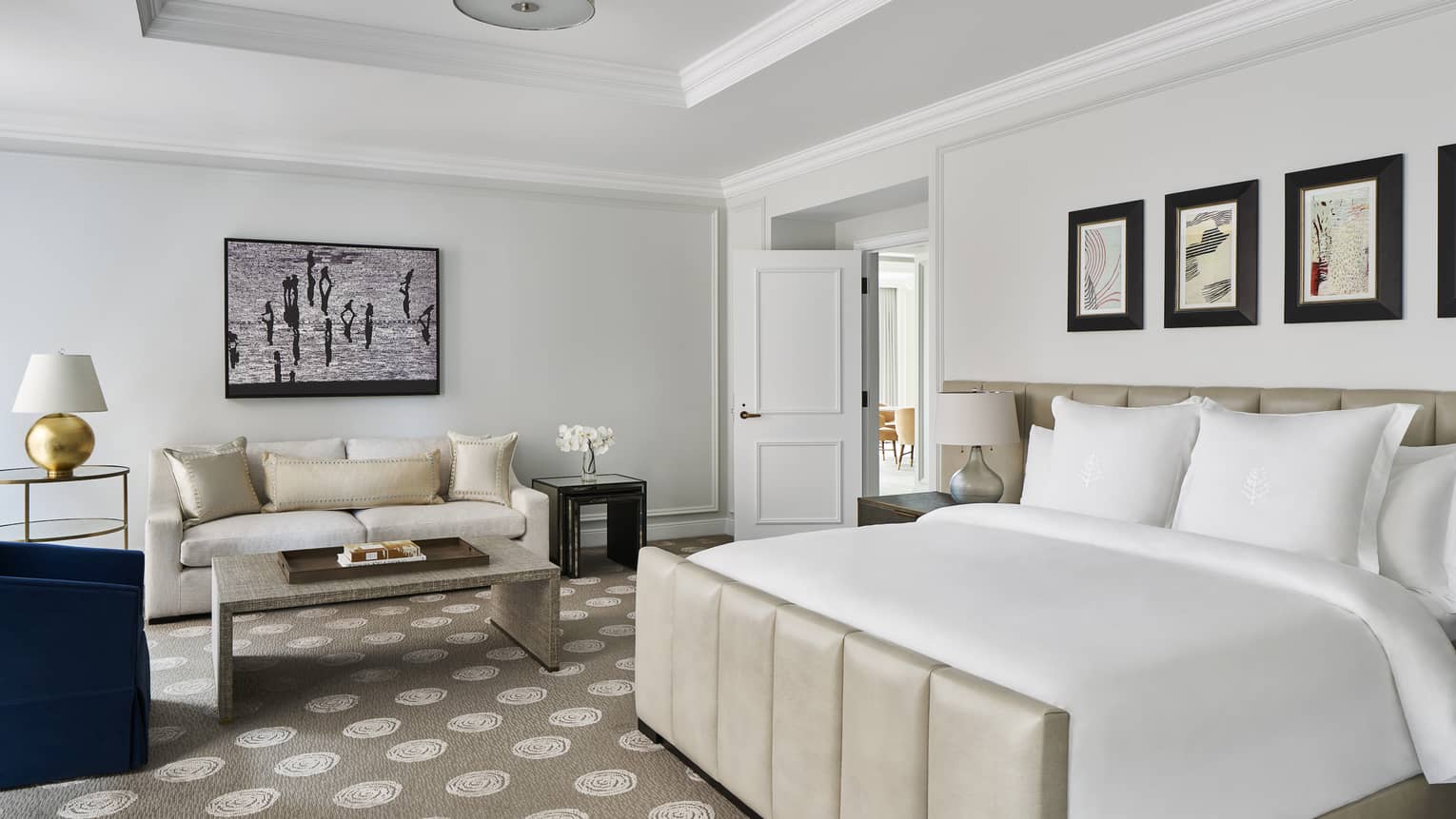 A hotel room with a large bed, sofa, coffee table and art on the walls.