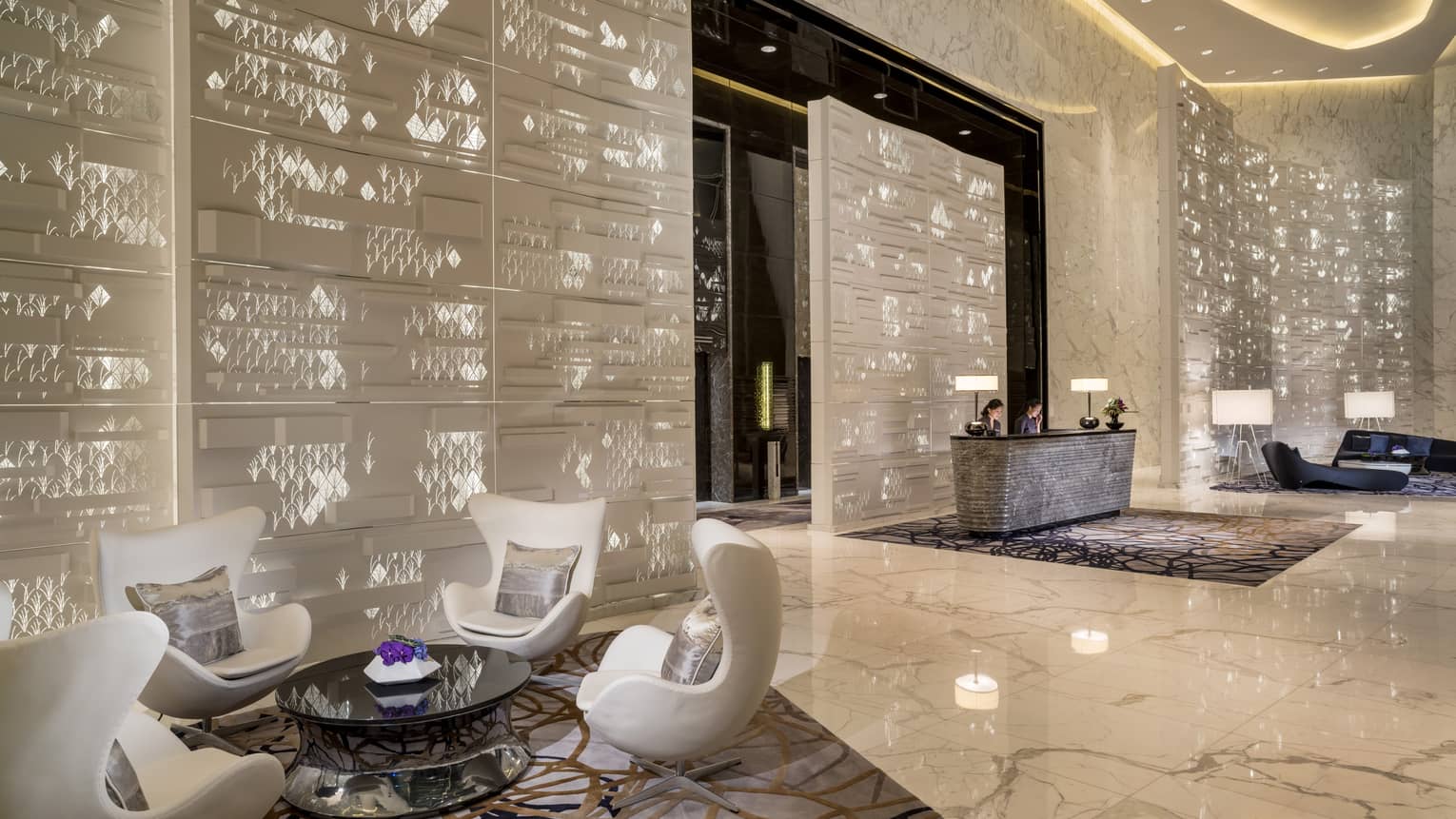 Four white mid-century style armchairs around glass table in lobby with white decorative panels, marble
