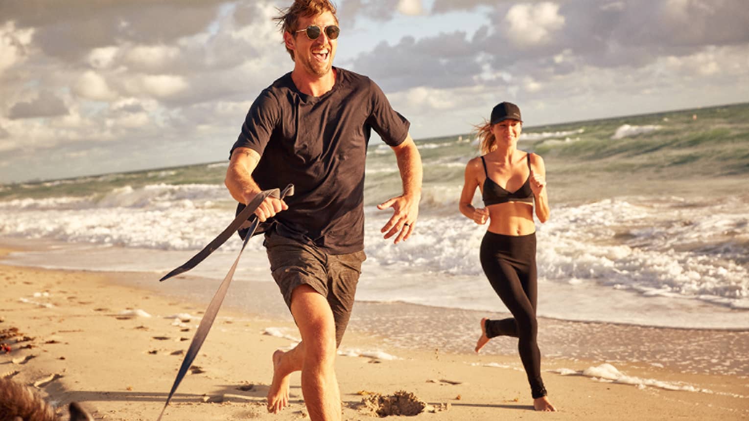 Man and woman jog along the beach with their dog