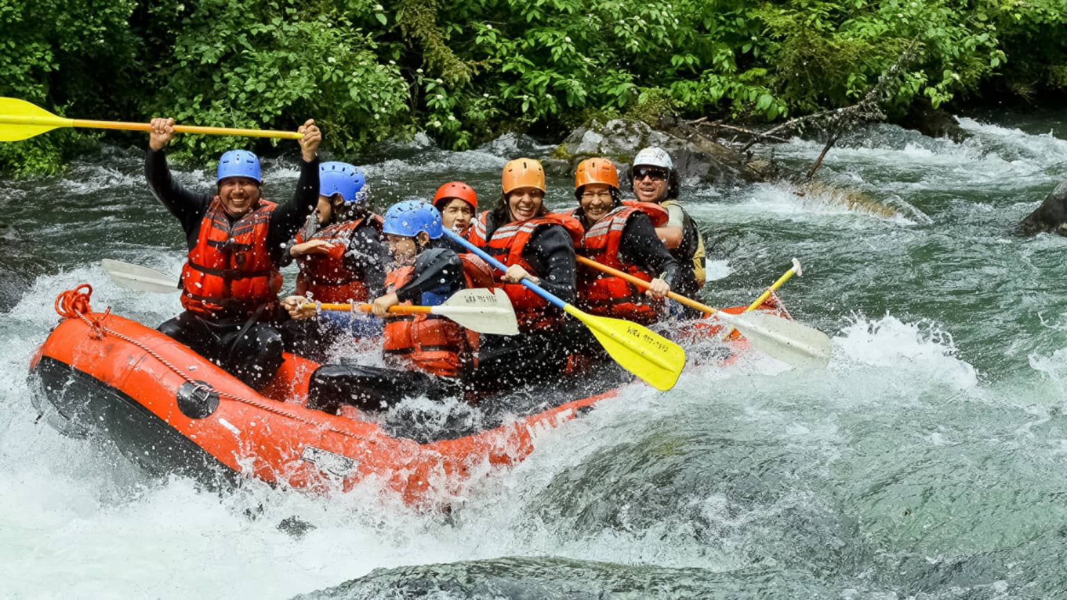 Smiling family wearing life jackets, helmets on white water raft on river rapids 