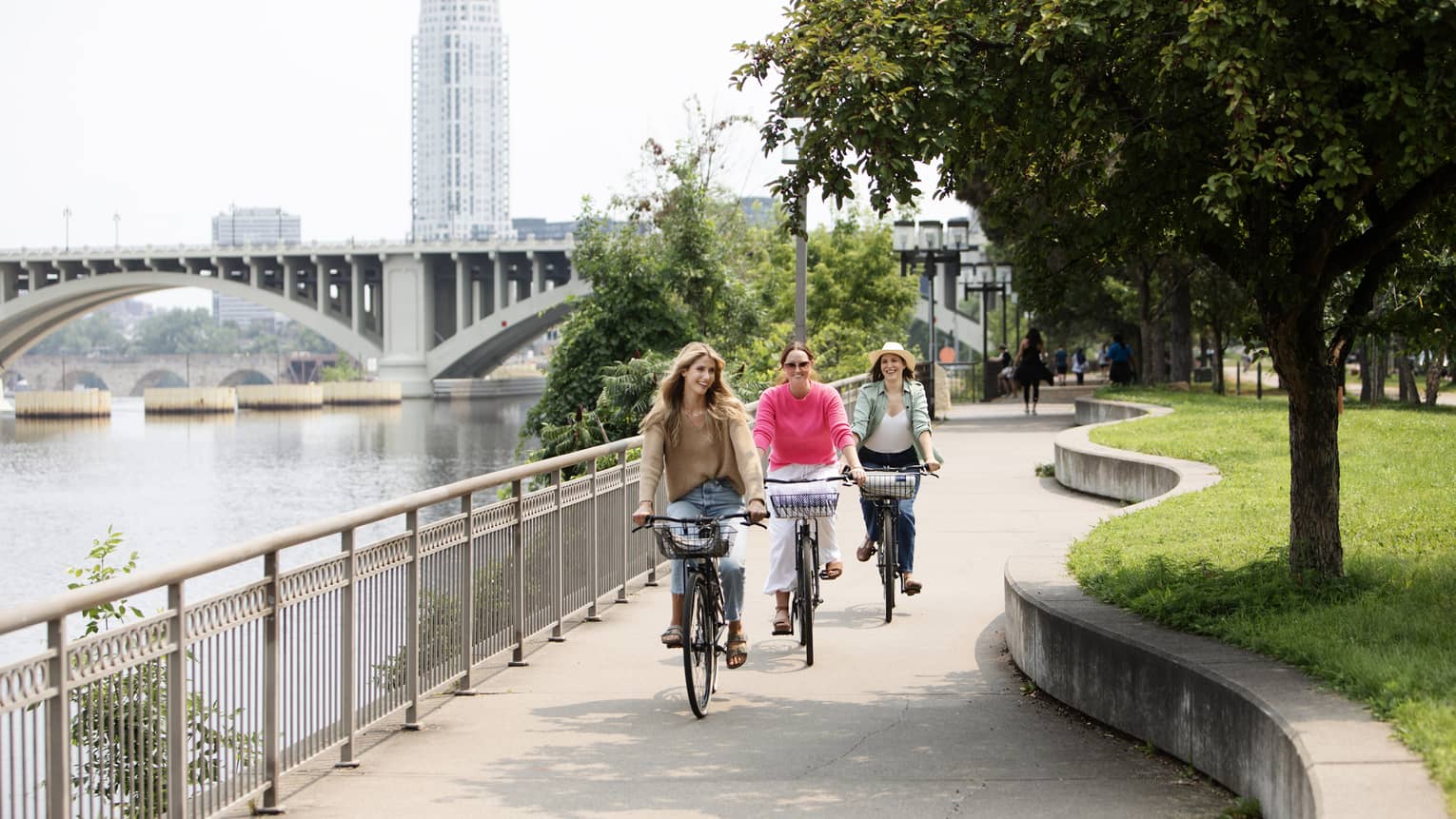 Three guests riding bicycles on the sidewalk near the lake and bridge