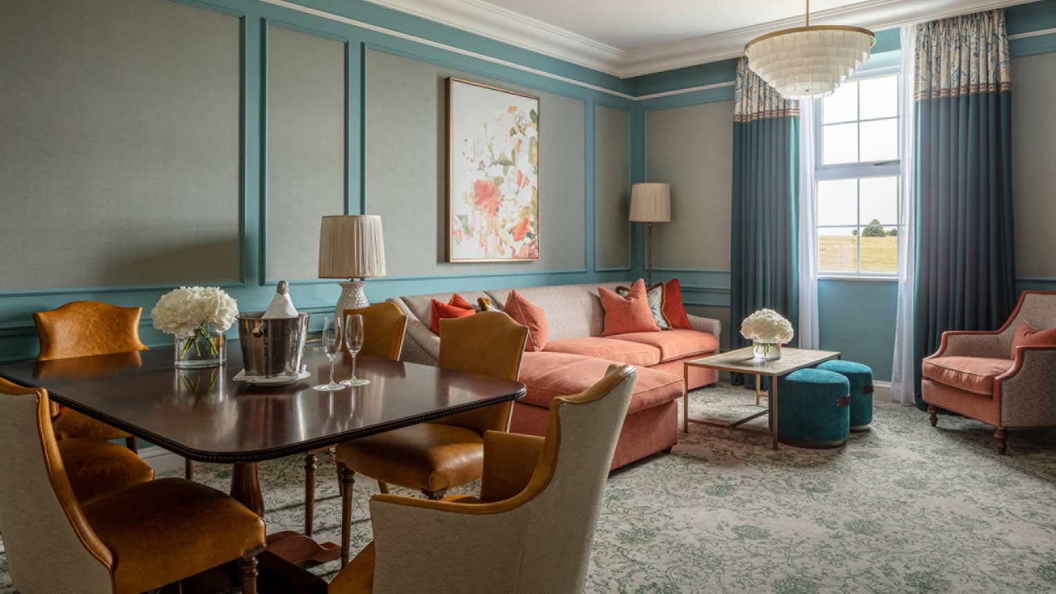 Guest room lounge area with red sectional sofa, coffee table, accent chair, rectangular dining table with six chairs, paisley carpeting, window with blue drapes