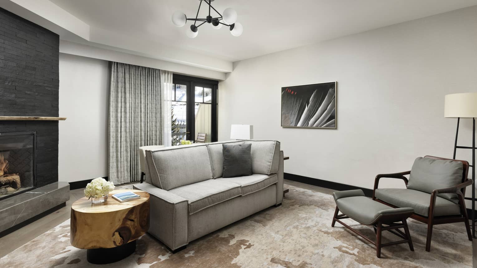 Living room with small grey sofa, arm chair and ottoman, wooden side table
