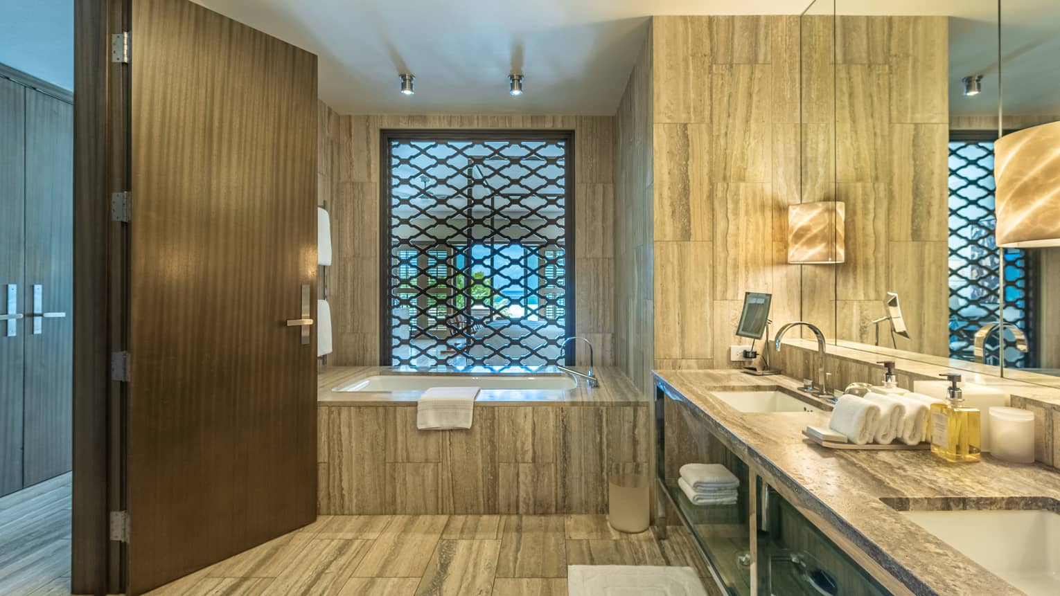 Contemporary bathroom of a resort guest room, featuring double vanity and deep soaking tub next to a latticed opening that separates bedroom from bathroom