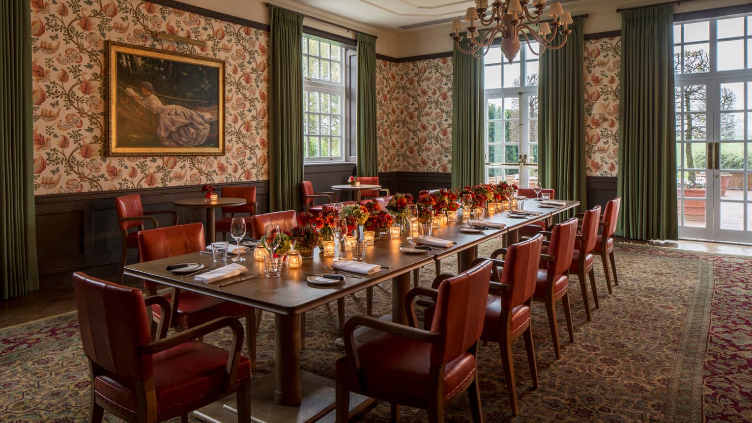 Long private dining table with candles, red flowers by corner windows, tall ceilings, floral wallpaper