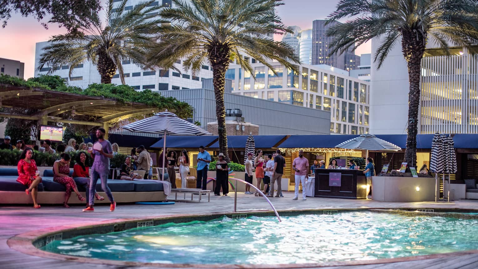 People socialize on patio under palm trees around small outdoor swimming pool