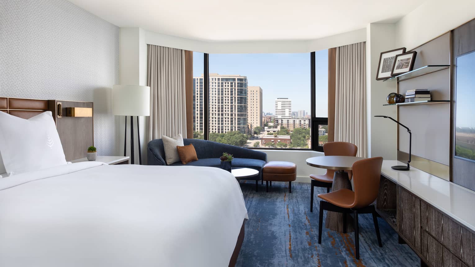 Hotel room with king bed, dark blue chaise lounge, table and two leather chairs, blue carpeting