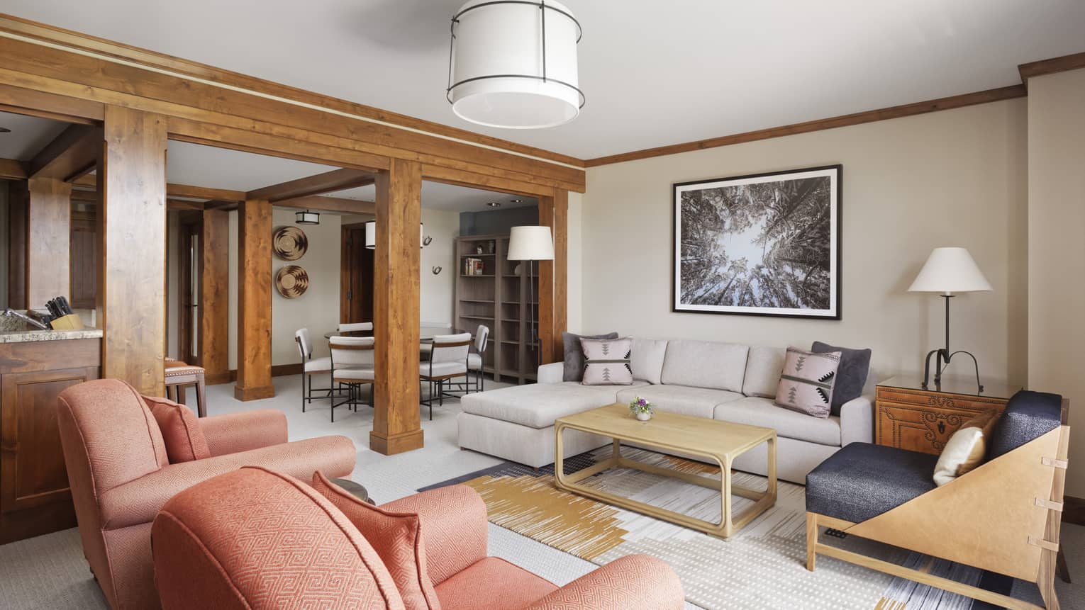 Living room with a sofa, two arm chairs and wooden beams separating dining area