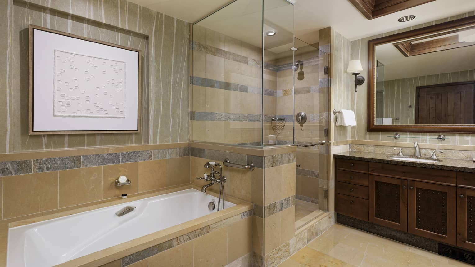Luxury resort bathroom with a bathtub, glass-enclosed shower, vanity, mirror, dark wood accents and framed artwork