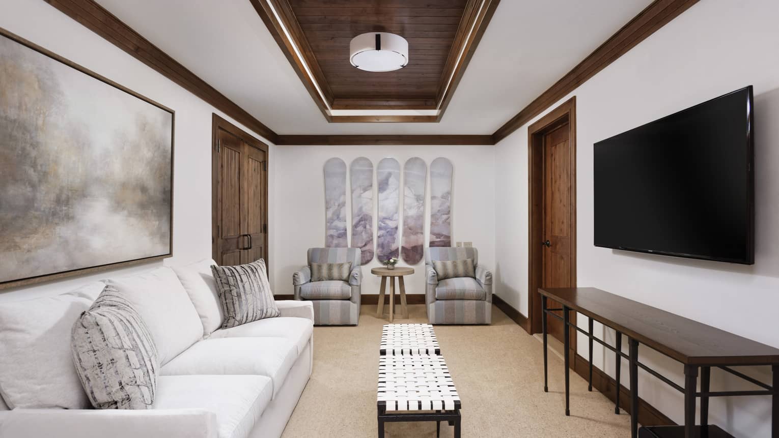 Guest room living area with cream sofa and twin striped armchairs, rectangular coffee table, wall-mounted flat screen TV, wooden accents