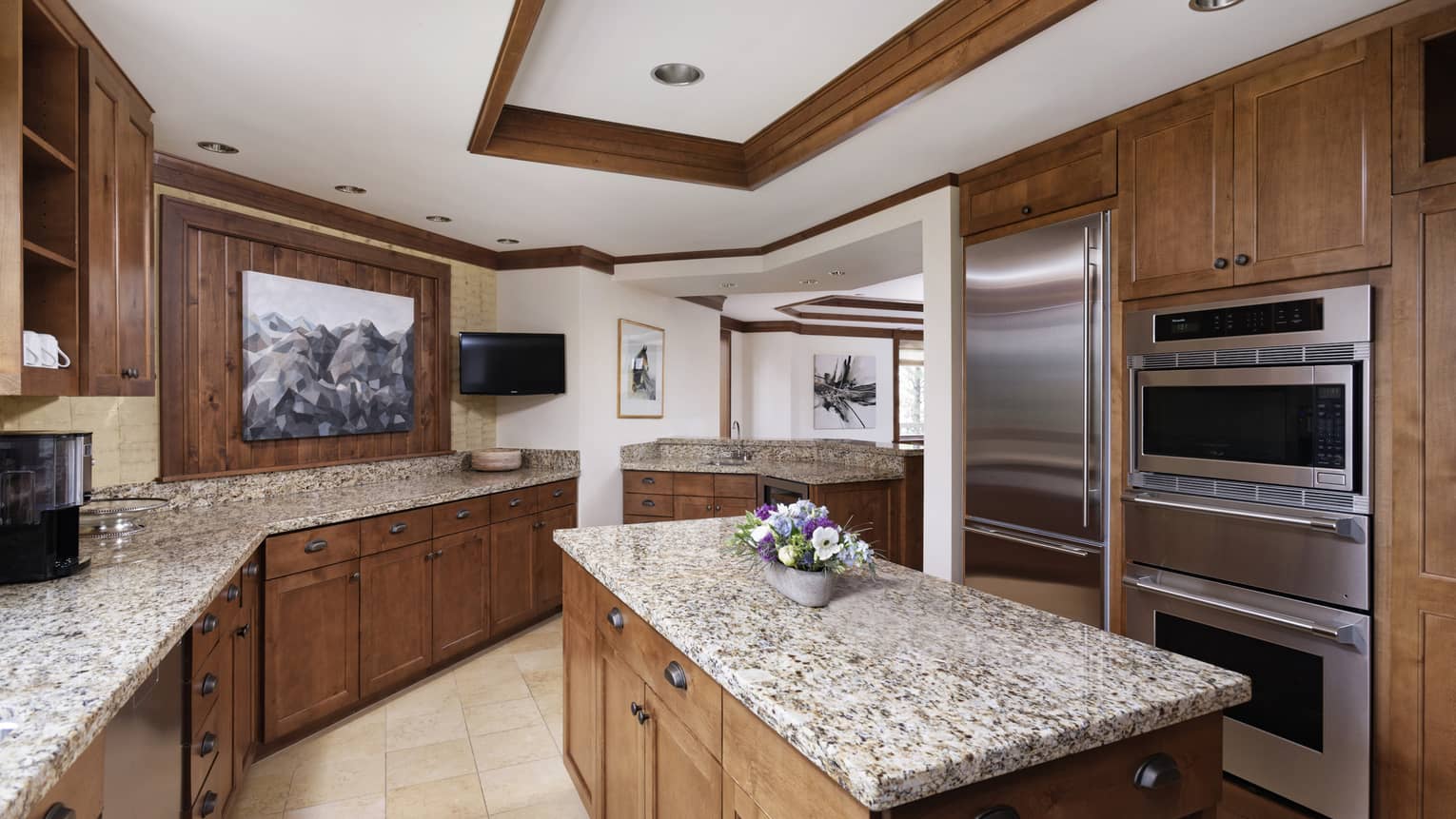 Luxury resort kitchen with dark wood cabinets, island, granite countertops, stainless steel appliances, TV and decorative artwork 