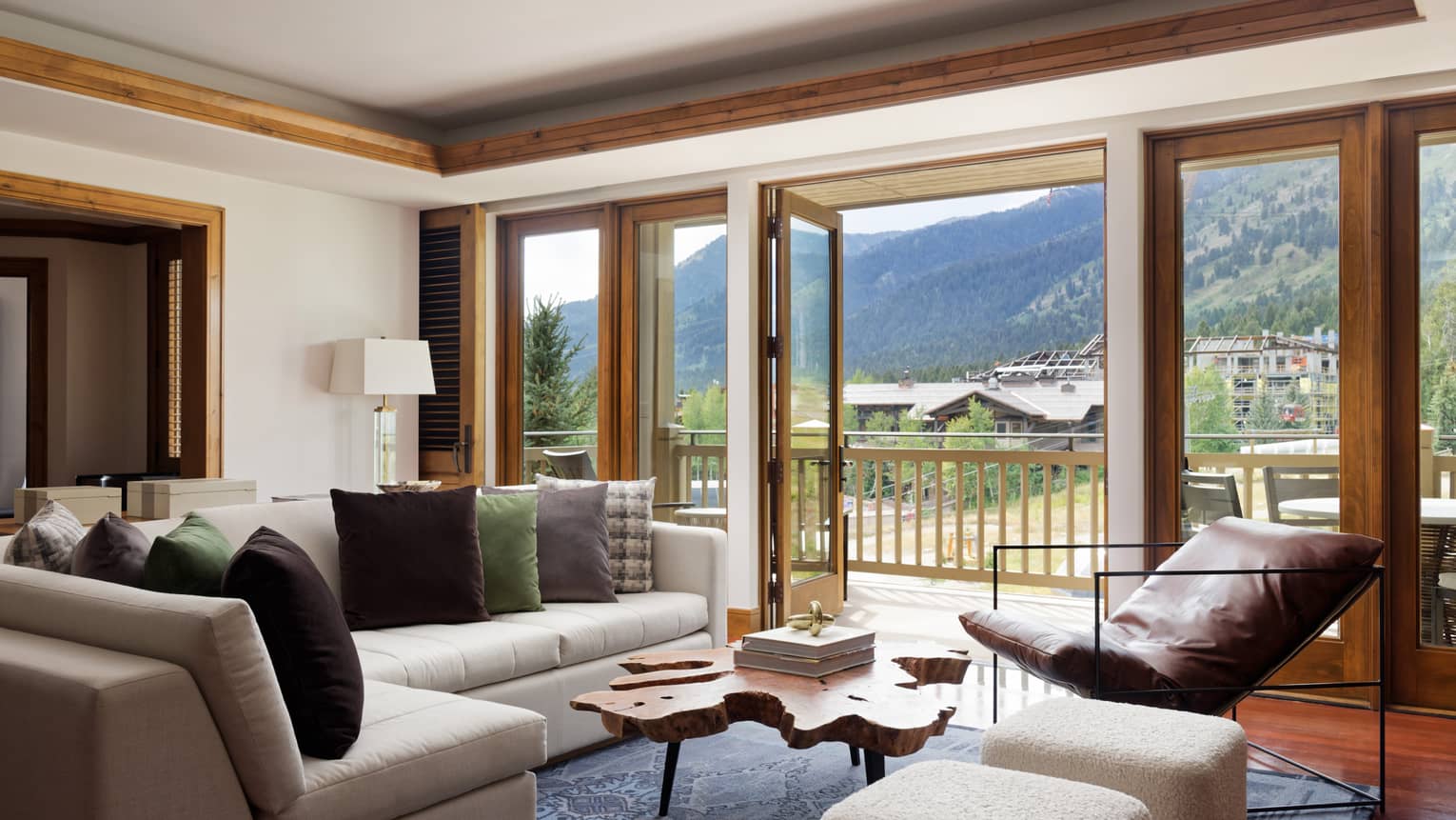 A room with a large sofa, coffee table, chair and large window looking out at mountains.
