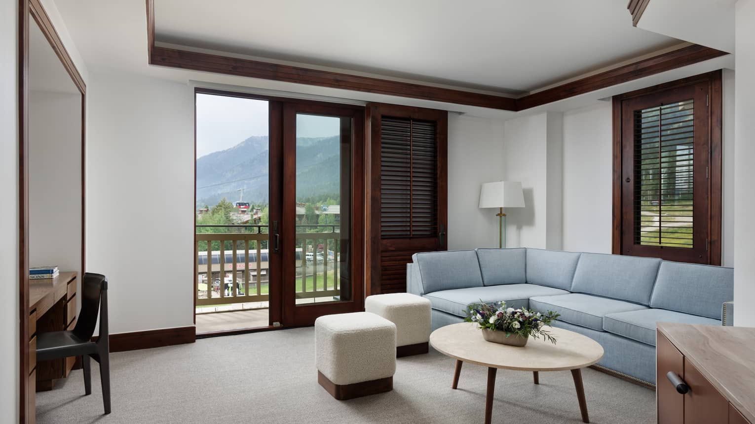 Living room with light blue sofa, two beige stools, coffee table and walk-out, mountain-view balcony
