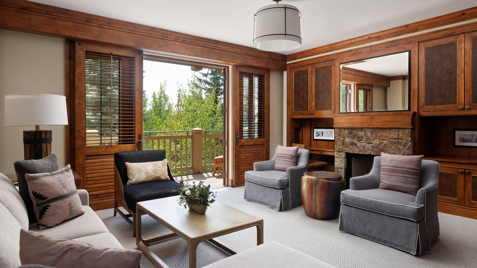 Mountain-chic living room with sofa, grey arm chairs, stone fireplace, mirror and walk-out balcony