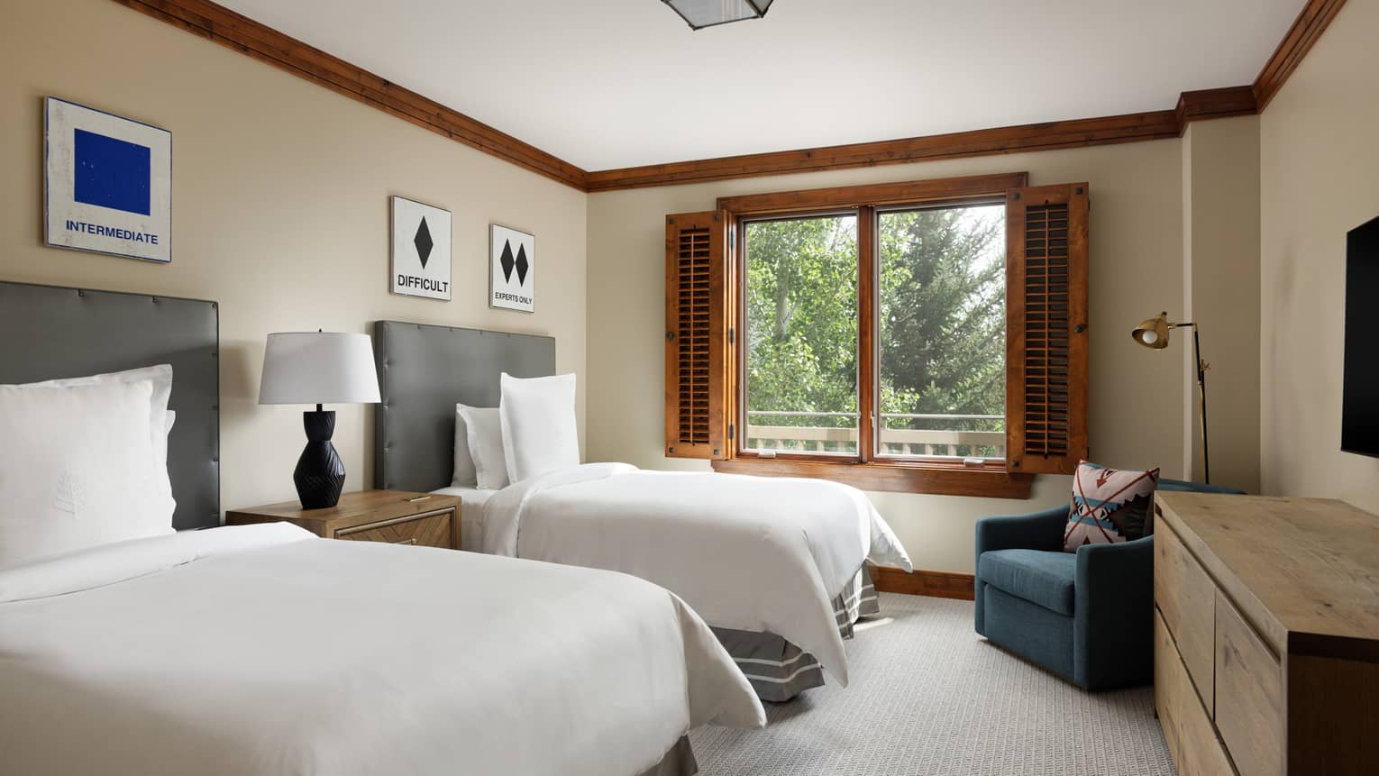 Bedroom with two beds, window with wooden shutters, dresser, armchair and ski-themed wall art